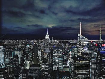 Illuminated buildings in city against cloudy sky