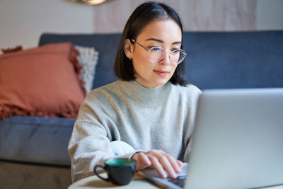 Young woman using mobile phone while sitting at home