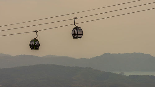 Overhead cable cars over mountains against sky