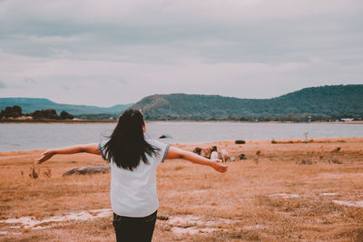 Rear view of woman standing on land by lake against sky