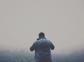 Rear view of man standing against sky during foggy weather