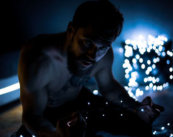 Shirtless man with illuminated string lights in dark
