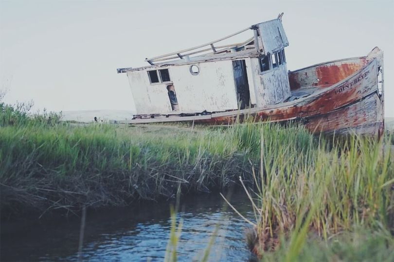 ABANDONED BOAT ON SHORE AGAINST SKY