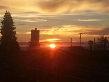 Silhouette of factory against sky during sunset