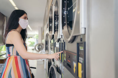 Beautiful woman with mask doing laundry at laundromat shop.