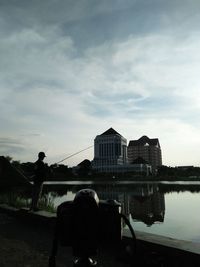 Silhouette buildings by lake against sky