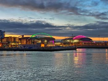 Illuminated ferris wheel in city against cloudy sky