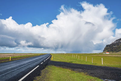 Scenic view of empty road amidst grassy landscape against sky