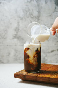 Cropped hand pouring milk in coffee on table