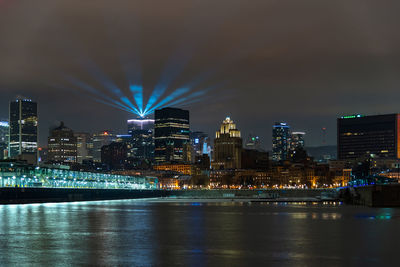 Illuminated buildings by river against sky at night