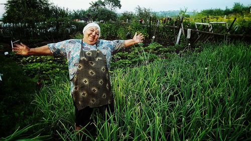 Senior woman with arms outstretched standing on grassy field