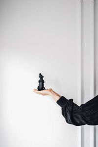 Woman in long sleeve black holding up a black rubber rat sculpture against white wall with moulding