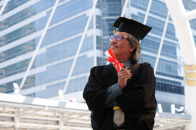 Businessman in graduation gown standing against office building