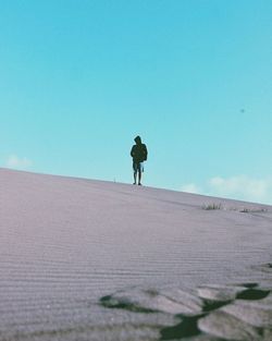 Man walking on sand dune against clear sky