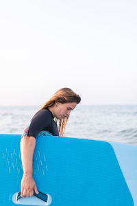 Side view of female in swimsuit standing with sup board in sea water in summer and looking away