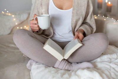 Midsection of woman reading book while sitting on floor