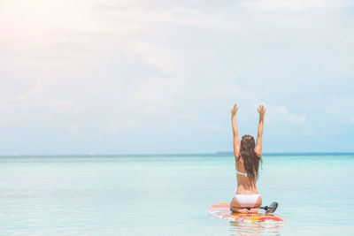 Rear view of woman with arms raised in sea against sky