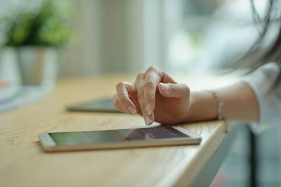 Cropped hand of woman using smart phone on table