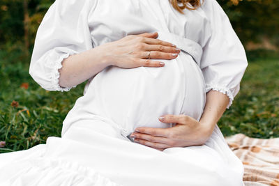 Close-up of a pregnant girl in a white dress in nature