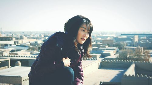 Portrait of young woman standing on roof against clear sky