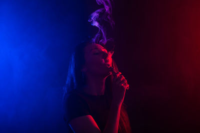 Young woman smoking cigarette against gray background