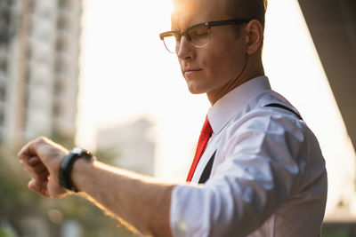 Businessman looking at wristwatch against sky