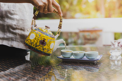 Woman hand pouring herbal tea into a pot on naturally blurred background.