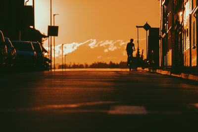 Silhouette man standing on street against sky during sunset