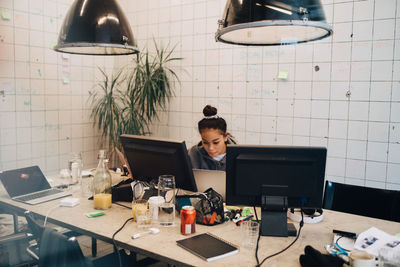 Confident young female programmer coding on laptop at desk in creative office