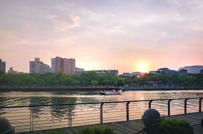 Scenic view of river by buildings against sky during sunset