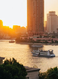 Boats in river by city against clear sky during sunset