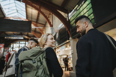 Smiling woman carrying luggage while talking with man at railroad station