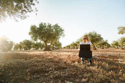 Woman using laptop while sitting at olive orchard