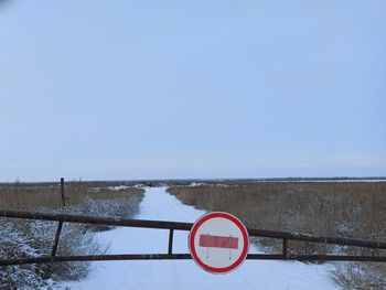 Road sign on snow covered field against clear sky