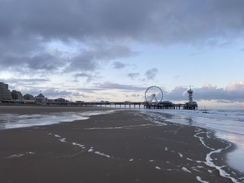 View of ferris wheel at beach against cloudy sky