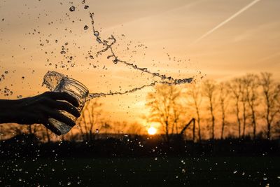 Cropped hand splashing water against sky during sunset