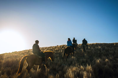 Men riding horses on field against sky