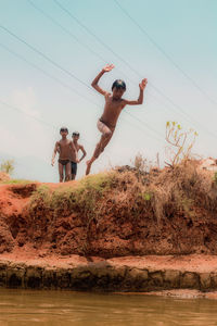 Men jumping on beach against sky