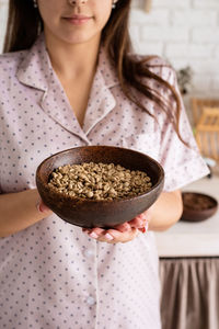  young woman in lovely pajamas making coffee at home kitchen holding bowl with coffee beans