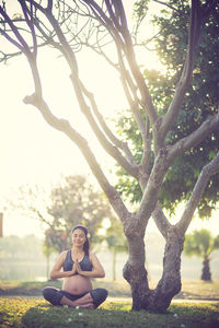 Woman doing yoga on field by bare tree