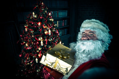 Portrait of man wearing santa claus costume holding christmas presents at home