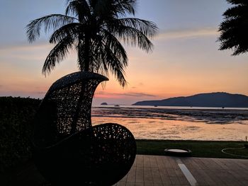 Silhouette palm tree by sea against sky during sunset