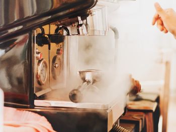 Cropped hand of person by steam emitting from espresso maker at cafe