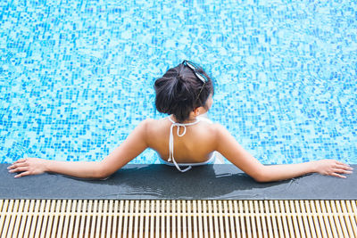 Rear view of woman sitting on swimming pool