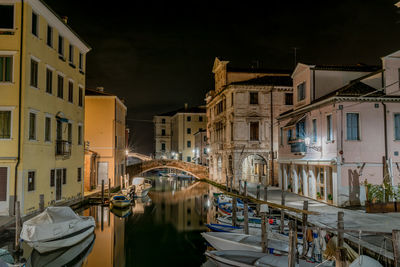 Boats moored on canal amidst buildings in city at night