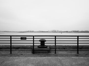 Empty bench by lake against clear sky