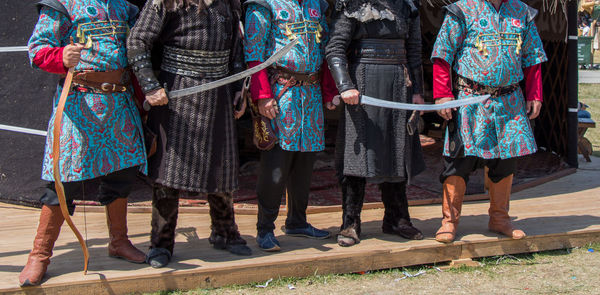 Low section of people in costume with weapon standing outdoors