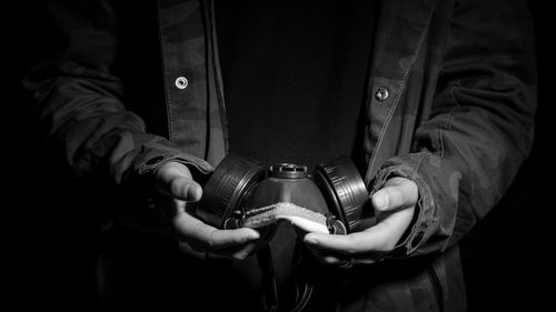 Midsection of man holding gas mask against black background