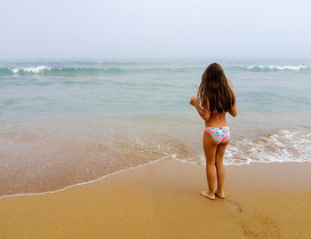 Rear view of woman standing at beach against sky