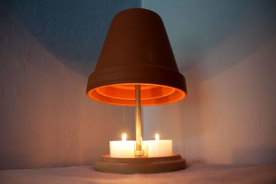 Close-up of illuminated lamp on table against wall